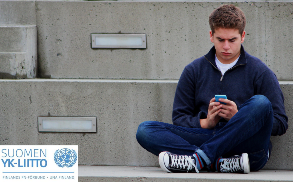 Poika istumassa kännykkä kädessä ja Suomen YK-liiton logo.